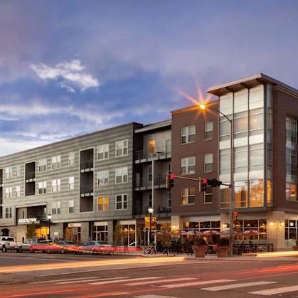 A modern building with a glass facade is illuminated by street lights at dusk.