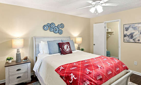 A bedroom with a bed covered in a red Alabama football bedspread.