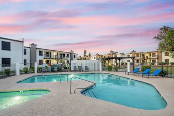 A swimming pool area with lounge chairs and apartment buildings in the background.