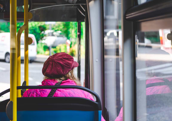A woman in a pink jacket and red hat is sitting on a bus. at The Alloy at Geneva, Vineyard, UT