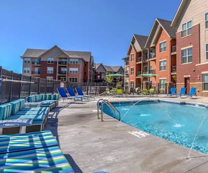 The large, turquoise outdoor pool with blue pool chairs, tables, and chairs with the apartments in the background at