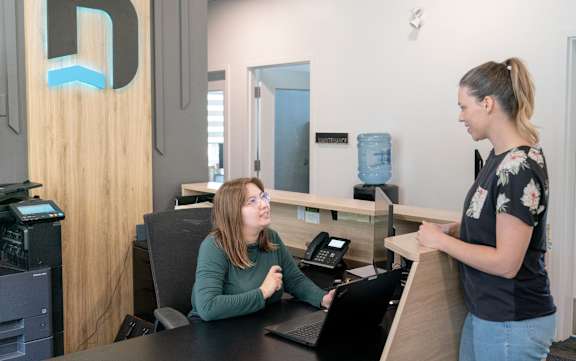A woman is standing at a reception desk talking to another woman who is seated.