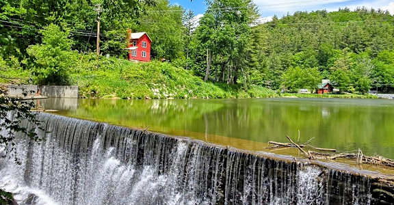 A small waterfall flows into a lake with a red house in the background.