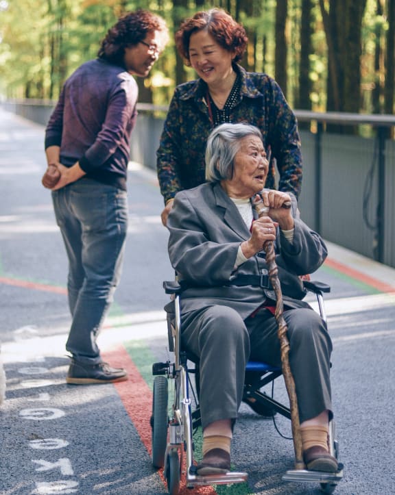an elderly woman in a wheelchair with two people standing behind herat Ovation at Meeker, Kent Washington