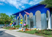 Thumbnail 22 of 23 - Jacksonville Mandarin Bay Apartments leasing office street view. Building is surrounded by grass and palm trees, balloons, and "Now Leasing" signs