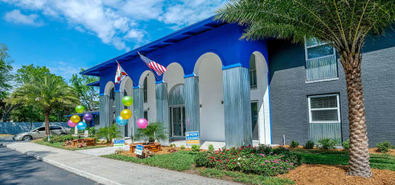 Jacksonville Mandarin Bay Apartments leasing office street view. Building is surrounded by grass and palm trees, balloons, and "Now Leasing" signs