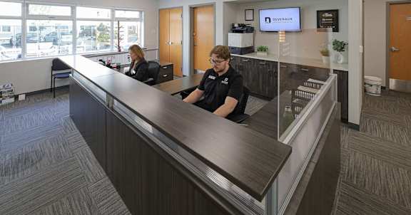 Two people sitting at a reception desk in a brightly lit office.