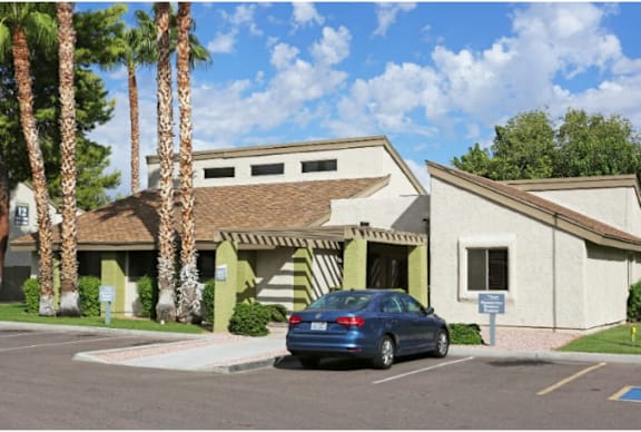 A blue car is parked in front of a building with a palm tree.