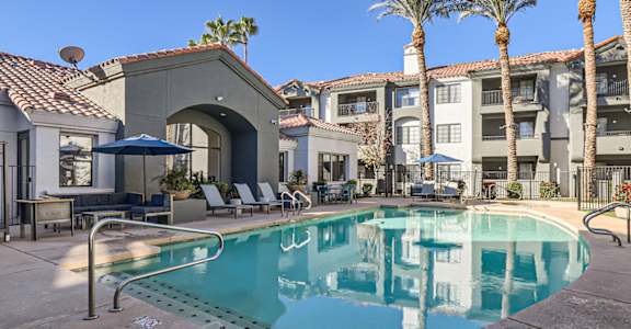 A pool surrounded by palm trees and lounge chairs.