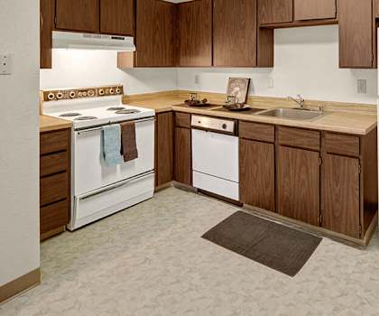A kitchen with wooden cabinets and marble countertops at Driftwood Apartments. 