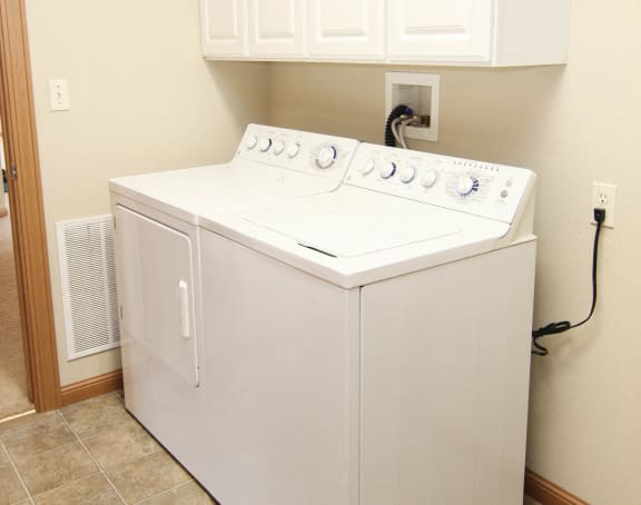 Side by side washer and dryer with storage cabinets above in laundry room
