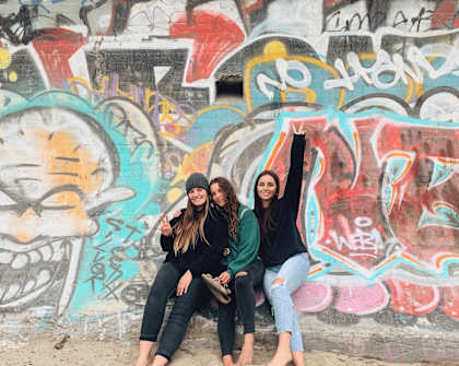 three women sitting on a wall in front of a graffiti covered wall