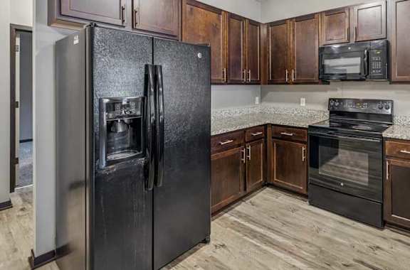 A kitchen with a black refrigerator and brown cabinets.