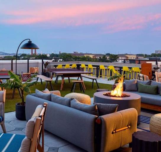 a rooftop lounge with couches and tables and a fire pit