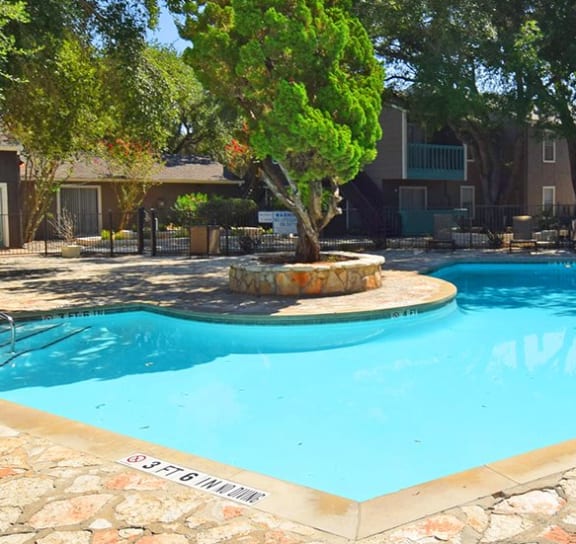 a swimming pool with a fountain and trees in the background