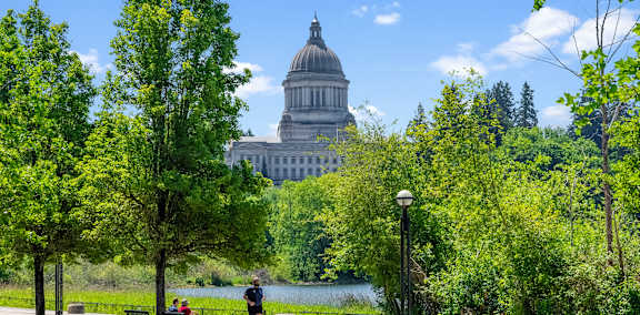 A man is walking on a bridge with a beautiful view of a white building in the distance.