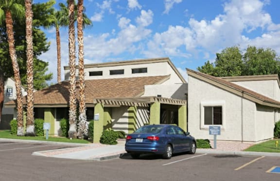 A blue car is parked in front of a building with a palm tree.