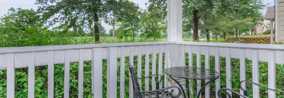 a small table and two chairs sit on a porch with trees in the background
