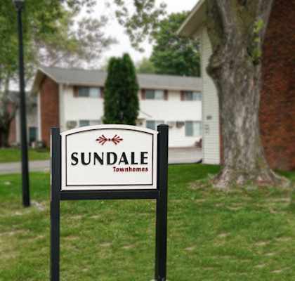 A sign for Sundale townhomes stands in a grassy area.