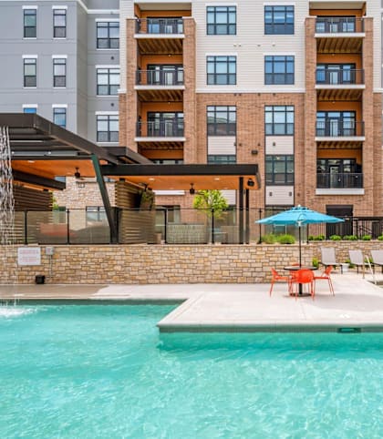 A swimming pool in front of a building with a patio area.