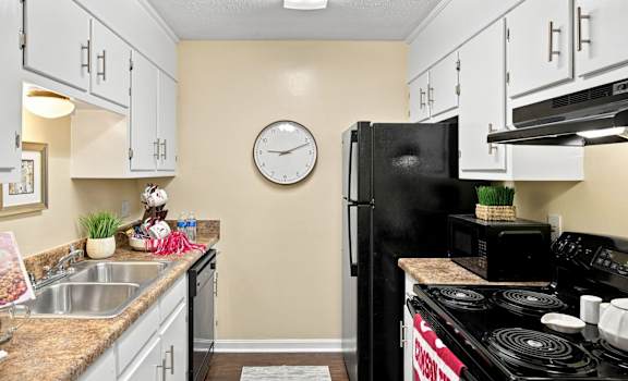 A kitchen with a black refrigerator and a clock on the wall.