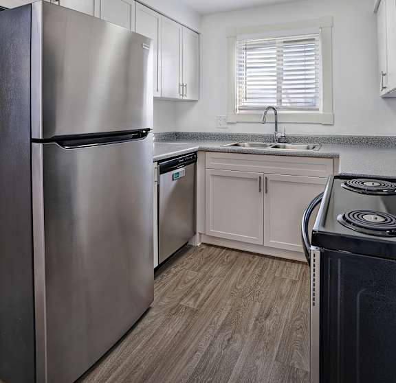 A modern kitchen with a stainless steel refrigerator and wooden flooring.