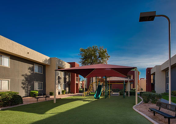 A playground area with a slide and a canopy is surrounded by buildings.