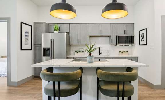 A modern kitchen with a white island and two green chairs.