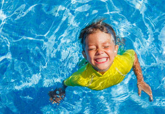 Child Swimming in Pool and Smiling