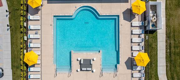 A large rectangular pool surrounded by yellow umbrellas and lounge chairs at Aventura at Wentzville I & II Apartments, Wentzville, MO
