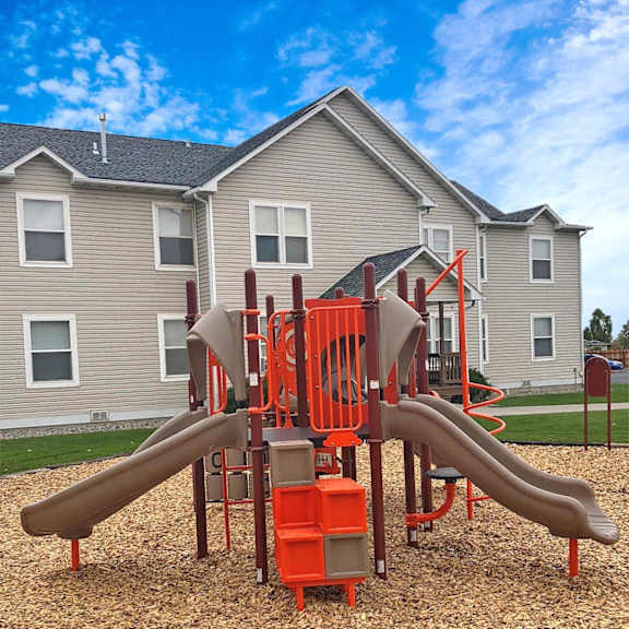 A playground with a slide and a play structure in front of a grey building.