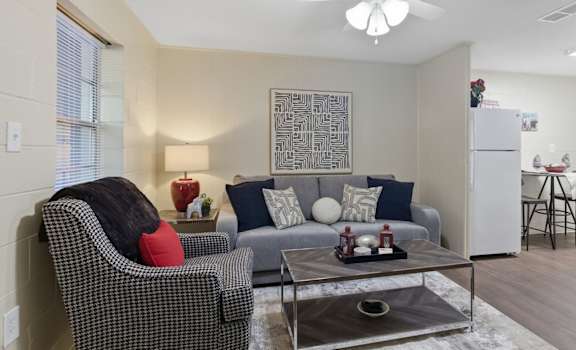 A living room with a grey sofa, a black and white checkered chair, a coffee table, and a ceiling fan.