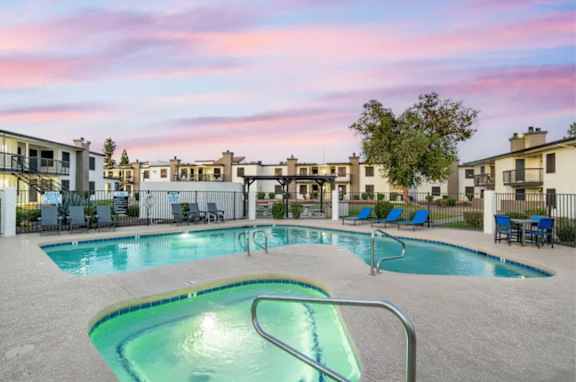 A swimming pool surrounded by lounge chairs and apartment buildings in the background.