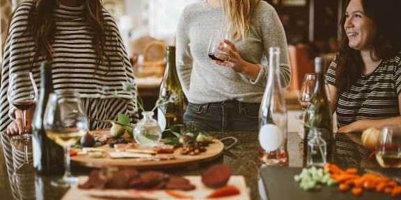 Three women are sitting at a table with wine glasses and food.