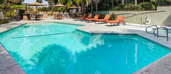 a swimming pool with lounge chairs and umbrellas in front of a building