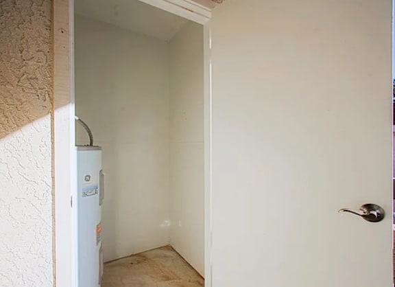 A white door is open to a room with a white wall and a white fridge.