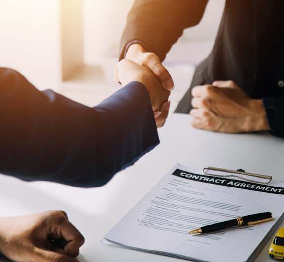 Two people shaking hands over a contract agreement.