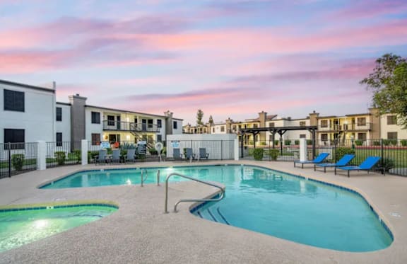 A swimming pool area with lounge chairs and apartment buildings in the background.