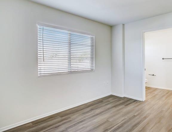 a bedroom with white walls and wood flooring and a door to a closet