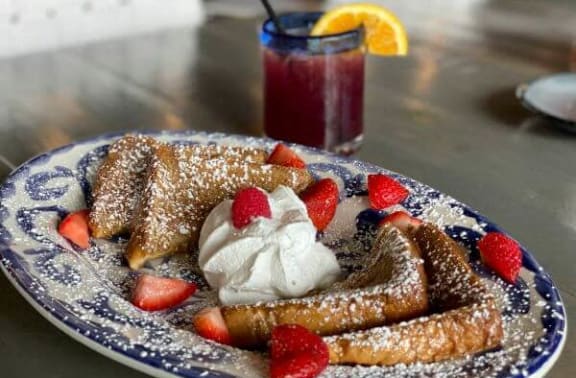 a plate of pancakes with whipped cream and strawberries and a drink