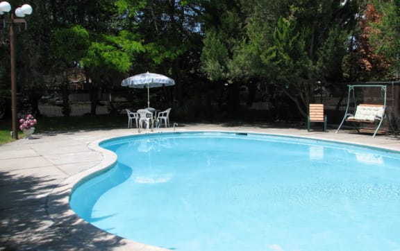 Swimming pool with umbrella seating, swing bench, surrounded by manicured lawn and large green trees. at Laurel Park, Twin Falls, ID 83301