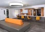 Thumbnail 19 of 23 - Fifteen 50 apartments Las Vegas clubhouse with modern orange chairs at a bar in front of orange accent wall and grey wood inspired flooring.