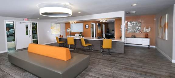 Fifteen 50 apartments Las Vegas clubhouse with modern orange chairs at a bar in front of orange accent wall and grey wood inspired flooring.