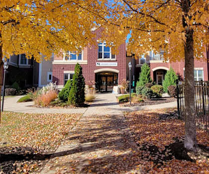 The entrance to the leasing office in a brick building with a sign above the door surrounded by fall leaves at Van Buren Place Apartment Homes. 