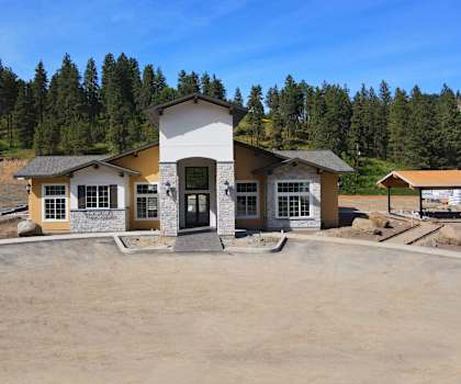A house with a brown roof and a white door is surrounded by a dirt lot.