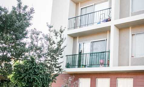 A white building with balconies and windows is surrounded by greenery.