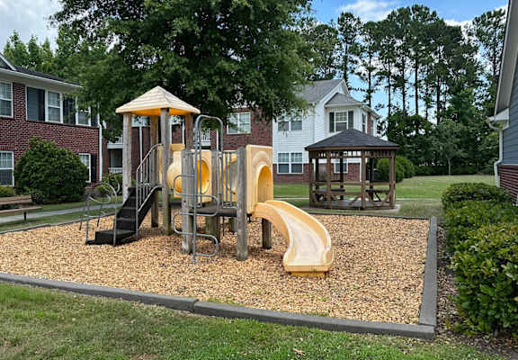 A playground with a yellow slide and a brown wooden structure.
