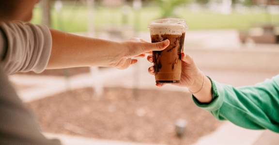 A person in a green shirt is passing a cup of coffee to another person.