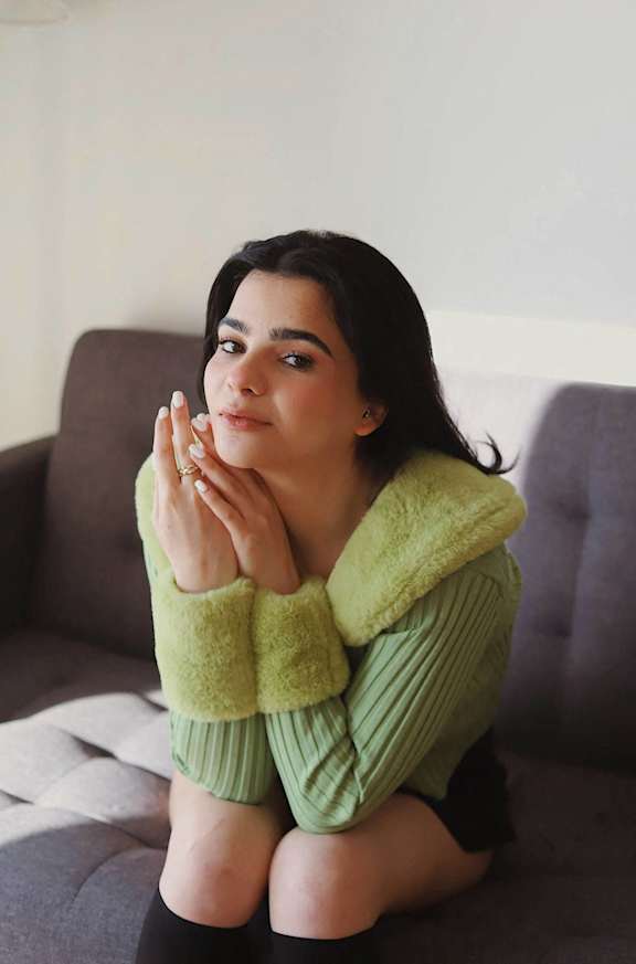 A woman in a green sweater and shorts is sitting on a grey couch.