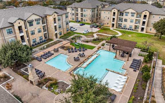 A large swimming pool surrounded by a grassy area and apartment buildings. at The Royce at 8100, Austin, TX, 78729